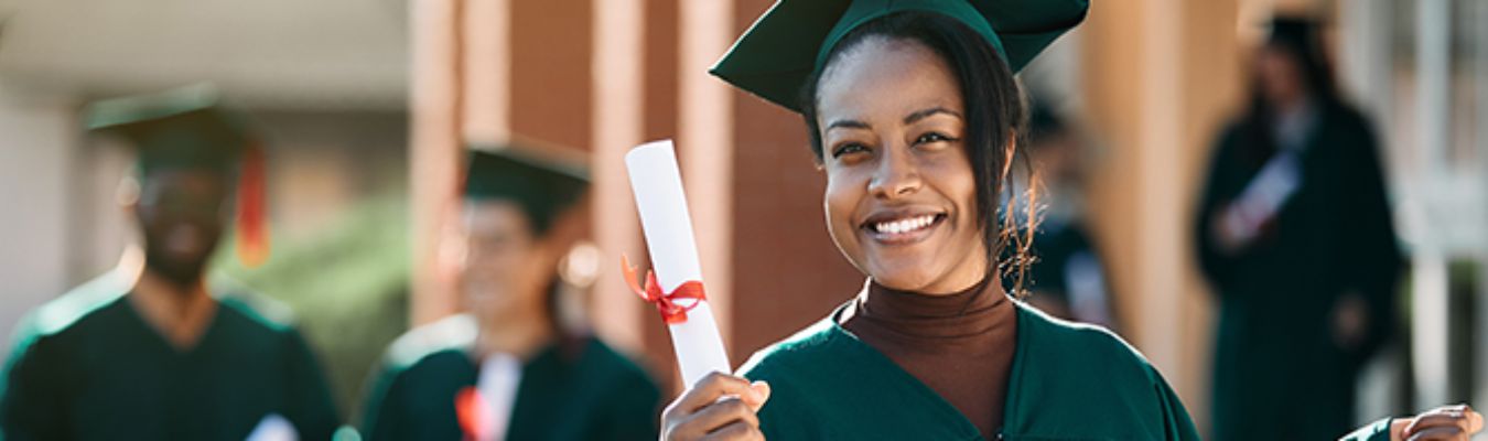 A student holding a scroll wearing a graduation gown with a smile
